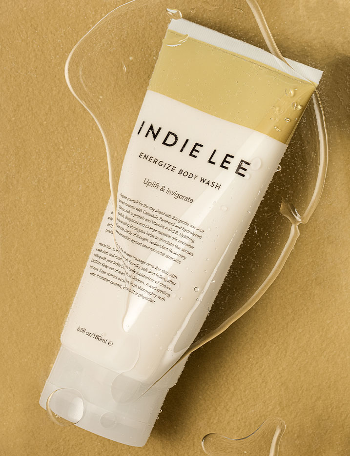 Bottle of Indie Lee brand Energize Body Wash displayed underwater with air bubbles collecting over the bottle.