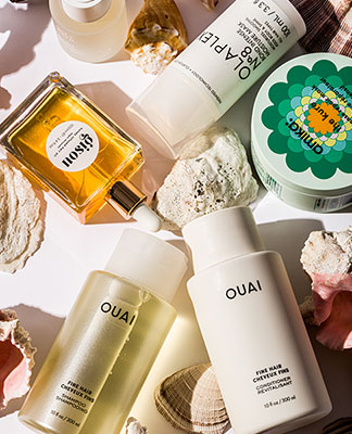 An assortment of beauty products displayed next to seashells. The Beauty Shop. Shop Now.